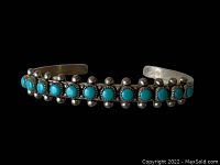 Front view of sterling silver cuff bracelet with turquoise stones on black background.