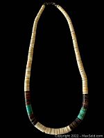Full view of beige heishi shell disc bead necklace with turquoise and dark brown bead sections and metal clasp on black background.