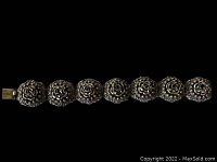 Top view of ornate antique bracelet showing seven large circular coin silver segments each featuring a raised central rose design with detailed surrounding floral motifs, clasp visible on one end.