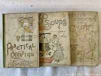 Three 1880s cookbooks by Thomas J Murrey displayed together. Covers have decorative artwork related to cooking.