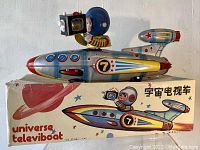 Front view of the Universe Televiboat toy placed on its original box showing the rocket design, astronaut figure holding a TV camera device, and color details.
