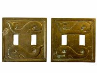 Pair of vintage brass double light switch plates with embossed whale designs, showing patina and discoloration.