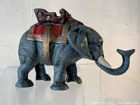 Front side view of the cast iron elephant bank showing the trunk lifted and the saddle paint details.
