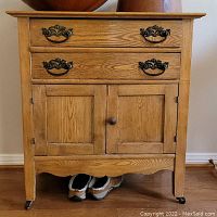 Front view showing two drawers with metal handles and two doors with a wooden knob on caster wheels, displaying natural oak grain.