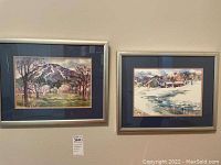 Two framed watercolor paintings hanging side by side on a wall; both with metal frames and dark blue mats.