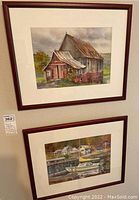 Photo showing both watercolor paintings hanging on wall, one above the other, both framed in wooden frames with mats.