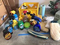 Photo showing collection of various vehicle cleaners, spray bottles, containers, buffing mitts, sponges, paper towels, and a yellow crate.