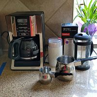 Mr. Coffee drip coffee maker, Bodum Bistro grinder, French press, and stainless steel pots displayed on a countertop