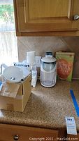 Photo showing both Cuisinart food processor and Black & Decker juicer on kitchen counter with recipe books behind.