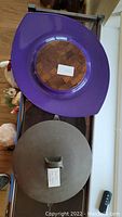 Top view of purple resin oval serving platter with wooden center and metal-lidded casserole beneath
