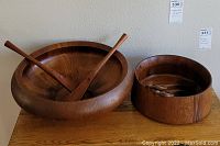 Both teak salad bowl sets, larger and smaller, displayed on a wooden table side by side