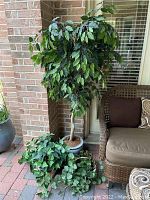 Full view of the set showing one tall faux tree in ceramic pot and two baskets of faux greenery near outdoor seating area.