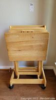 Front view of three wooden folding TV trays nested in the wooden storage stand on wheels.