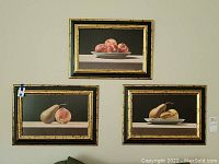 Three framed fruit prints arranged on a wall showing peaches and pears on plates.