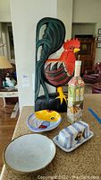Photo showing large painted wood rooster, oil dispenser, coordinating ceramic bowl with broken rim, and vintage pottery bowl and covered butter dish on the counter.
