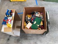 Wide shot of open box filled with varied Lego bricks and base plates with some assembled pieces on top.