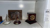 Shelf with all items: wooden nautical plaque with metal relief, two glass yacht figurines (one under dome), Howard Miller clock with hygrometer