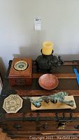 Full view of all five oriental motif decor items arranged on wooden trunk, including compass box, elephant candle holder, metal bowl, dragon sculpture, and zodiac tile.