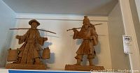Two Asian fisherman clay statues on wooden bases displayed on a shelf