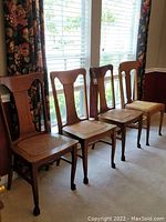 Set of four vintage wooden chairs with cane inset seats seen from the side, showing uniform style and condition.