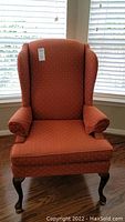 Front view of the rust-colored wingback chair showing the upholstery and shape.
