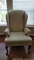 Full view of cream upholstered wingback armchair with patterned fabric with Queen Anne style wood pad feet.