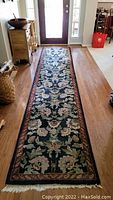 Full view of long floral wool runner rug on hardwood floor showing overall pattern, colors, fringed ends, and length.