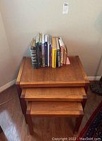 Photo showing the three teak nesting tables stacked with books on top