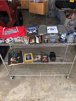 Photo showing a wire rack with various items including dvds, a Zippo lighter case, collectible toys and mugs, model airplanes, and a red Coca-Cola cooler bag.