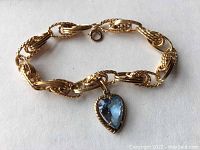 Full view of gold chain bracelet with heart-shaped blue charm on white background
