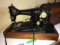 Side view of the black Singer sewing machine mounted on wooden base with visible gold branding and sewing components