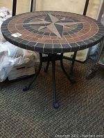 Side view of the round bistro table showing stone look top and black metal frame with curved legs.