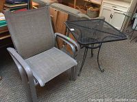 Two sling fabric chairs and one black metal mesh table arranged on carpet indoors.