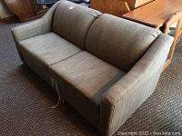 Green upholstered loveseat seen from an angle, showing the seating area, armrest, and overall condition with minor wear.