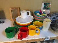 Colorful dishware on white table including green, red, yellow mugs, and colorful bowls and plates