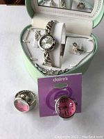 Silver-colored Nexuss clip-on earrings, necklace, wristwatch set inside heart-shaped jewelry case; two additional silver ring watches in front (one tagged Claire's)