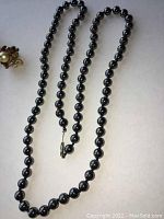 Photo of the full black beaded necklace showing the spherical beads and clasp, highlighting the overall style and construction.