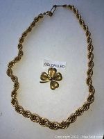 Full view of a gold filled four-leaf clover brooch and a twisted rope chain necklace on a white background.