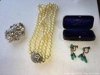 Photo showing all four jewelry items: gold chain necklace, pearl necklace with rhinestone clasp, turquoise clip-on earrings in a case, and rhinestone brooch pin