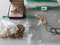 Overview of the gold filled chain in a bag, Monet gold color pearl bracelet in a bag, plus two small cords and the Ariki lizard brooch in box