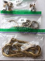 Photo showing three plastic bags containing jewelry pieces: top has two pairs of clip on earrings, middle has a pair of silver-toned beaded earrings, bottom has a long twisted gold colored necklace. The green zipper bags are labeled 42 and 44A.
