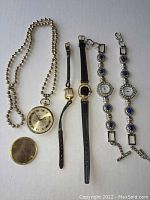 Five watches laid out on a surface including two silver bracelet watches with blue rhinestones, one pocket watch, a Gerrard Perregaux watch, and a vintage Jovenia watch.