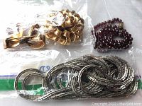 Photo showing two Monet gold-tone brooches in a plastic bag, a dark red/beaded necklace and a long white metal linked Les Bernard necklace