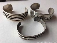 Three sterling silver cuff bracelets with distinct patterns laid on a flat surface.
