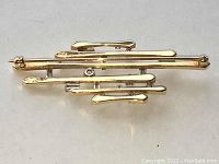 Overhead view of entire brooch showing layout of six uneven length yellow gold bars.