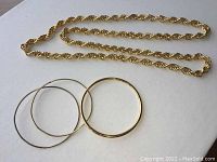 Photo of gold colored twisted rope chain necklace with three gold colored bangles on white surface.