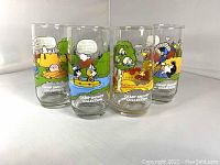 Front view of four glasses arranged in a row showing colorful cartoon scenes with Peanuts characters.