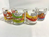 Four vintage glass mugs with Garfield comic strip illustrations laid in a row showing full side views.