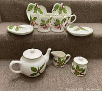 Overall shot of 12-piece vintage brunch set - teapot with lid, creamer, sugar bowl with lid, 4 plates, 5 mugs, all decorated with holly leaves and berries pattern.