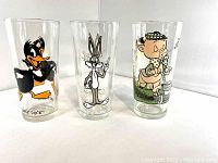Photo showing the front side of each of the three collectible glasses featuring Daffy Duck, Bugs Bunny, and Porky and Petunia Pig characters.